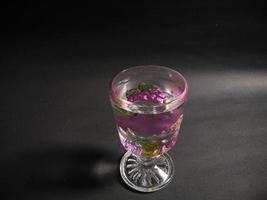 un verre transparent à motifs de fruits rempli d'eau minérale sur fond noir.