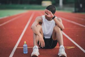 Athlètes coureur sport homme bouteille d'eau au repos fatigué et assoiffé s'entraînant sur une piste de course dans un stade. courir l'eau potable d'entraînement. concept de course d'homme de sport. photo