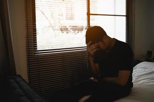 homme asiatique triste souffrant d'insomnie dépressive éveillé et assis seul sur le lit dans la chambre. silhouette homme déprimé tristement assis sur le lit dans la chambre à coucher, concept de dépression photo