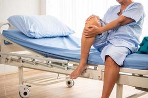 homme patient asiatique ressentant de la douleur au genou dans la chambre d'hôpital. photo