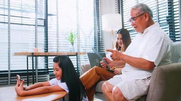 grand-père, mère et fille utilisent la technologie sans fil tout en se relaxant dans le salon. une famille asiatique profite de la technologie mobile moderne dans sa maison. photo