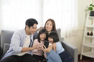 famille asiatique avec enfants tenant un smartphone et faisant un appel vidéo à la maison photo