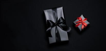 vue de dessus d'une boîte cadeau noire avec des rubans rouges et noirs isolés sur fond noir. photo