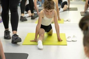 l'enfant s'entraîne dans le studio de danse dans le hall sur le tapis, fait des exercices d'étirement et des abdominaux, s'assoit sur les fentes. travailler sur soi et son corps depuis l'enfance, se dépasser photo