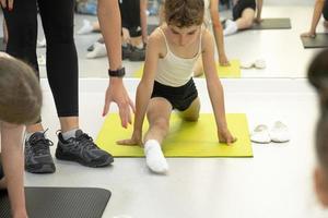 l'enfant s'entraîne dans le studio de danse dans le hall sur le tapis, fait des exercices d'étirement et des abdominaux, s'assoit sur les fentes. travailler sur soi et son corps depuis l'enfance, se dépasser photo