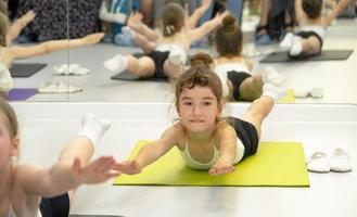 l'enfant s'entraîne en salle de sport sur le tapis, fait des exercices d'étirement et des abdominaux, de la gymnastique et de l'entraînement physique général. travailler sur soi et son corps depuis l'enfance, se dépasser photo