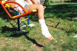 les jambes des enfants sont bandées dans du plâtre - pieds nus sur une balançoire. équipement traumatique, blessure infantile, ecchymose, entorse, fracture photo