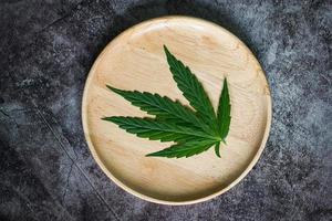 feuille de cannabis sur une plaque en bois, feuilles de marijuana plante sur fond sombre, cannabis nourriture nature herbe cbd thc concept photo