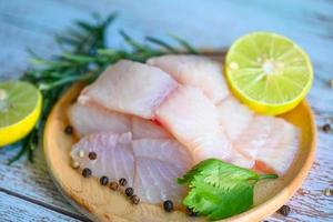 filet de poisson sur une assiette en bois avec des ingrédients pour la cuisson, filet de poisson pangasius cru frais avec herbes et épices poivre noir citron citron vert et romarin, viande poisson dolly poisson tilapia poisson-chat rayé photo