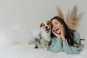 concept de personnes et d'animaux. joyeuse jolie jeune femme exprime son amour pour le chien, passe du temps libre avec son animal de compagnie, s'allonge ensemble sur le lit, regarde tendrement l'animal, ne s'ennuie pas avec un véritable ami fidèle photo