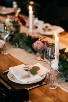 table de souper servie pour la fête. assiettes, bougies, couteaux, fourchettes sur table en bois décorée de branches de verdure. table de banquet de restauration. long bureau festif. concept de célébration et de prise de nourriture photo