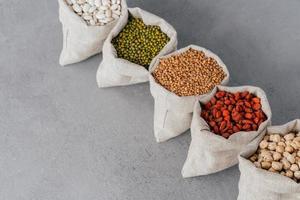 assortiment de grains sans gluten dans des sacs en tissu de lin sur fond gris. sacs remplis de haricots rouges, de lentilles, de sarrasin, de goji et de garbanzo. céréales pour une alimentation saine photo