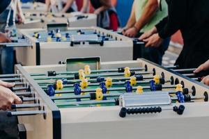 des amis masculins jouent au baby-foot avec beaucoup de chaleur, profitent de temps de loisirs ou de loisirs, veulent gagner. centre de divertissement. joueurs en plastique colorés sur un match de football photo