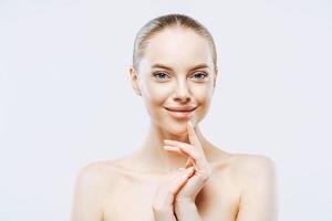 femmes, beauté, concept de soins de la peau. jolie femme brune souriante porte un minimum de maquillage, sourit agréablement, touche un teint doux et frais bien soigné applique des cosmétiques de soin de la peau isolés sur un mur blanc photo