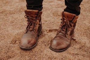 image d'un homme méconnaissable se dresse sur un sol sablonneux dans de vieilles chaussures shaggy en cuir marron avec lacets. chaussures pour hommes. tir en plein air photo