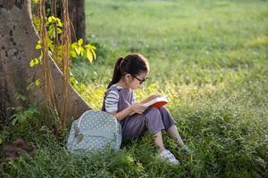 une jolie petite fille asiatique lisant un livre sous le grand arbre. photo