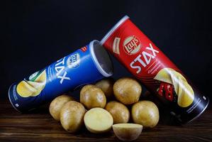 deux boîtes de chips se trouvent sur une table à côté de pommes de terre fraîches sur fond sombre. photo