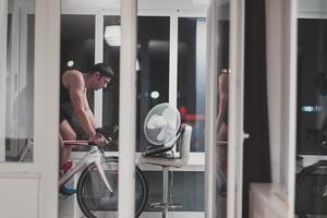 homme faisant du vélo sur l'entraîneur de la machine il s'exerce à la maison la nuit en jouant au jeu de course de vélo en ligne photo