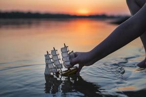 un garçon lance un bateau décoratif jouet au coucher du soleil. loisirs de plein air pour enfants en été. photo