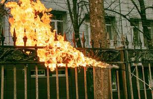 un travailleur nettoie la vieille peinture d'une clôture métallique en utilisant le feu. la main d'un homme tient un brûleur à gaz avec une flamme allumée photo