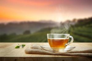 tasse chaude de thé et de feuilles de thé sur une table en bois avec le fond des plantations de thé photo