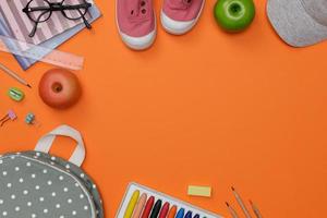 maquette vue de dessus des accessoires de l'éducation avec sac à dos, livres d'étudiants, chaussures, crayon coloré, lunettes, espace vide isolé sur fond orange, concept d'éducation et retour à l'école photo