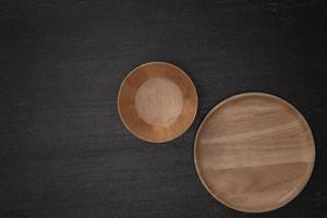 groupe de bols et assiettes ronds en bois vierges vides sur fond noir en pierre noire, vue de dessus du concept d'ustensiles de cuisine artisanaux traditionnels photo