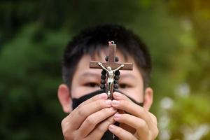 une croix en bois et un chapelet en bois sont tenus entre les mains d'une jeune prière catholique asiatique tout en priant dans le parc du temple. photo