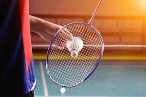 le joueur de badminton tient une raquette et un volant crème blanc devant le filet avant de le servir de l'autre côté du terrain. photo