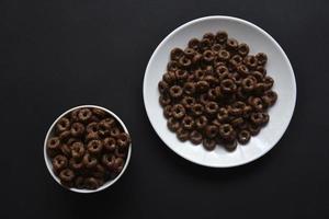 petit-déjeuner de cornflakes au chocolat et au miel sur des assiettes blanches sur fond noir. délicieux petit déjeuner de gros plan de cornflakes. photo