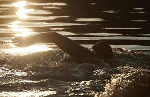 athlète de triathlon nageant sur le lac au lever du soleil portant une combinaison de plongée photo