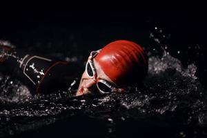 athlète de triathlon nageant dans la nuit noire portant une combinaison de plongée photo