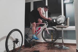 homme faisant du vélo sur l'entraîneur de la machine il s'exerce à la maison la nuit en jouant au jeu de course de vélo en ligne photo