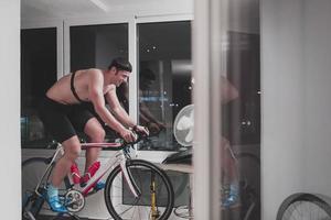 homme faisant du vélo sur l'entraîneur de la machine il s'exerce à la maison la nuit en jouant au jeu de course de vélo en ligne photo