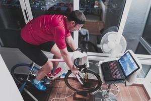 homme faisant du vélo sur l'entraîneur de la machine il s'exerce à la maison la nuit en jouant au jeu de course de vélo en ligne photo