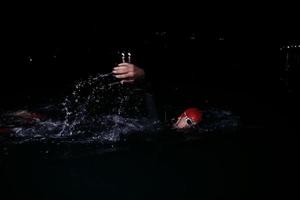 athlète de triathlon nageant dans la nuit noire portant une combinaison de plongée photo