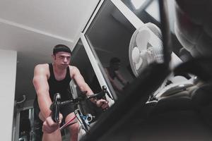 homme faisant du vélo sur l'entraîneur de la machine il s'exerce à la maison la nuit en jouant au jeu de course de vélo en ligne photo