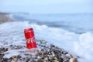 antalya, turquie - 4 juillet 2021 la boîte de conserve rouge coca cola originale se trouve sur de petits cailloux ronds près du bord de mer. coca-cola sur la plage turque photo