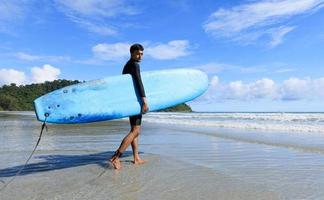 jeune homme en forme et corps ferme adolescent marchant dans la mer tenant une planche souple prête pour les sports extrêmes surfant sur les vacances à la plage et regardant vers l'appareil photo. photo