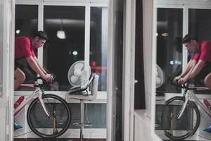 homme faisant du vélo sur l'entraîneur de la machine il s'exerce à la maison la nuit en jouant au jeu de course de vélo en ligne photo