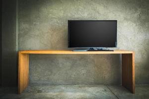 télévision lcd à plat sur table en bois dans le salon avec mur de béton grunge et parquet photo