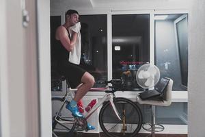 homme faisant du vélo sur l'entraîneur de la machine il s'exerce à la maison la nuit en jouant au jeu de course de vélo en ligne photo