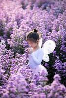 jolie petite fille qui sent les fleurs et porte un costume de fée de ballet magique dans le magnifique champ de fleurs violet de margaret. photo