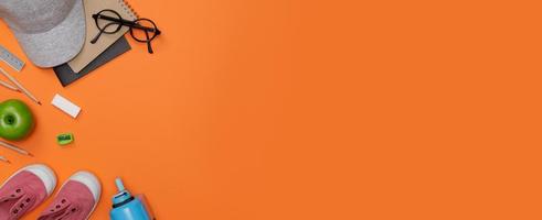 flatlay créatif de l'éducation table orange avec casquette, livres d'étudiants, chaussures, crayon coloré, lunettes, espace vide en studio tourné isolé sur fond de bannière longue orange, concept d'éducation photo