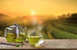 tasse à thé vert et cruches ou bocaux en verre. avec et sac de feuilles de thé vert sur la table en bois et le fond des plantations de thé photo