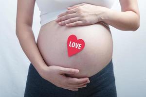 femme enceinte avec un seul coeur rose sur sa bosse de bébé. le tout sur fond blanc. photo