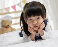 petite fille allongée sur le ventre et souriante, petite fille asiatique heureuse jouant sur le lit en bois dans sa chambre, concept de famille heureuse photo