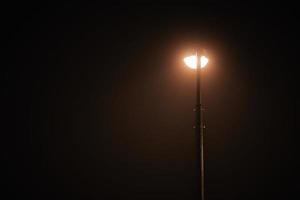 un lampadaire de nuit brille d'une faible lumière jaune mystérieuse à travers le brouillard du soir, l'espace de copie de gauche photo