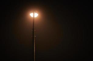 un lampadaire de nuit brille d'une faible lumière jaune mystérieuse à travers le brouillard du soir, l'espace de copie de droite photo