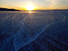 belle scène de coucher de soleil du lac baïkal en hiver, avec texture et motif pittoresque de traces de pneus sur la surface de la glace. photo